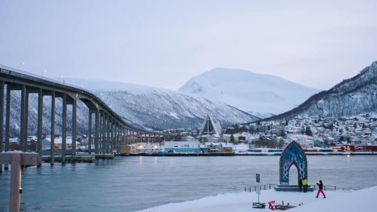 Fjellheim, bynære omgivelser og sjø i vinterlandskap med bro og kunstinstallasjon.
