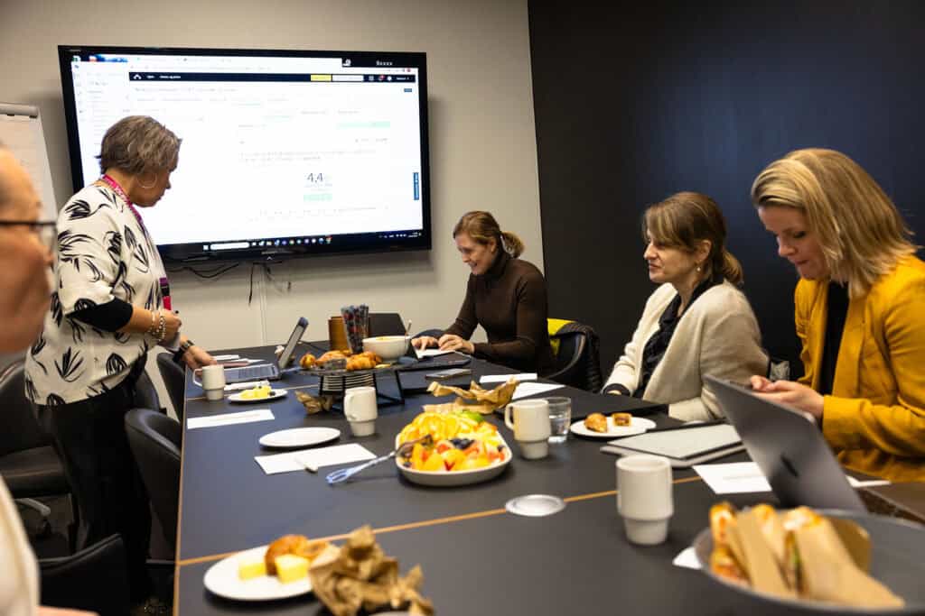 Kvinnelige ansatte i møte på kontor med digitale skjermer og frokostmat.