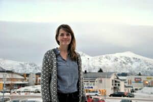 Frodig kvinne foran snødekte fjell og bylandskap i Tromsø, Norge, vinterstemning.
