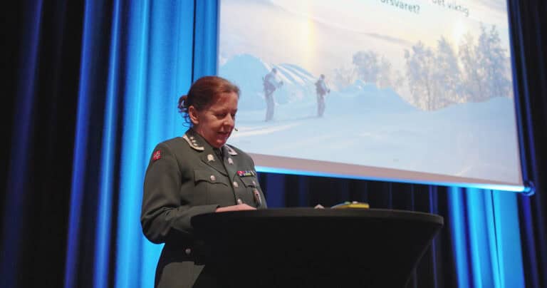 Kvinnelig foredragsholder i militæruniform foran presentasjonskjerm.
