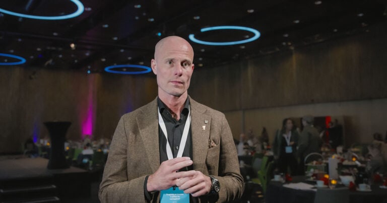 Mann i konferansemiljø med mørk bakgrunn og dekorative lysringer.