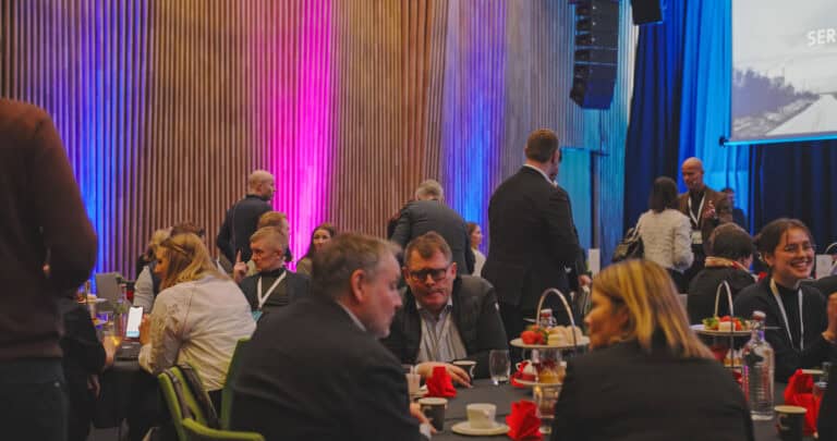 Møte i byrom med folk som snakker og spiser, i et moderne konferanselokale.