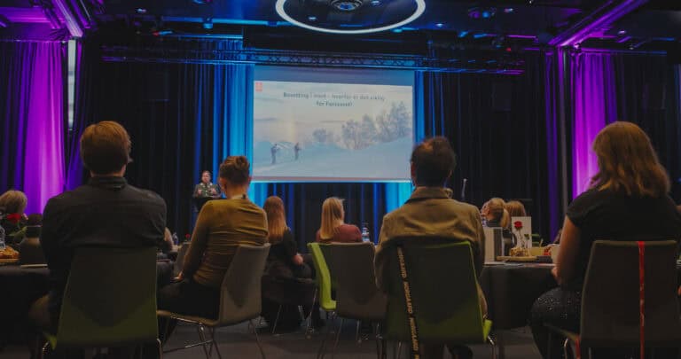 Publikum deltar på konferanse i Hjerterom for byrom med presentasjon på skjerm.