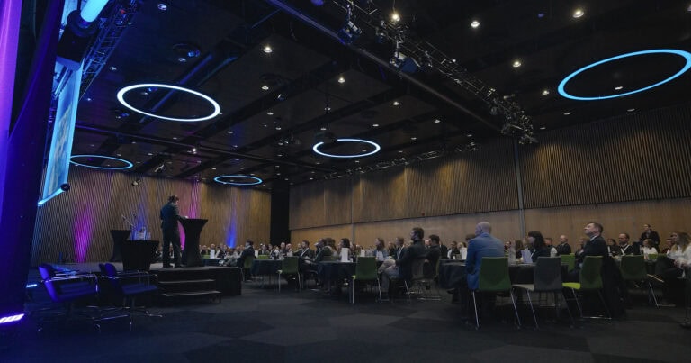 Møte i et stort, moderne auditorium med deltakere og presentasjonsområde.