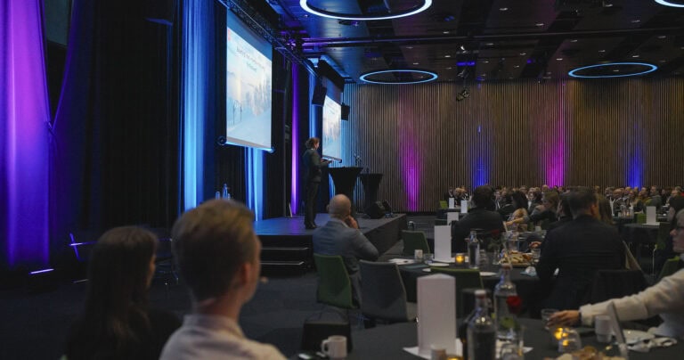 Profesjonell konferanse med presentasjon og publikum i et moderne auditorium.