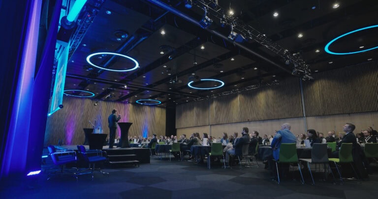 Konferanse i byrom med publikum og talere på scenen.