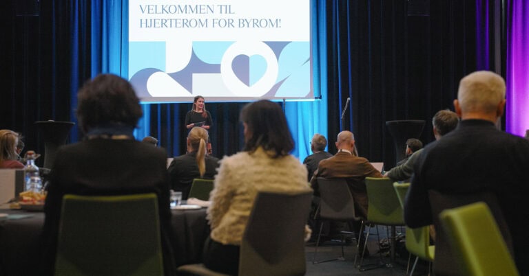 Publikum på konferanse i Hjerterom for byrom med presentasjon på skjerm.